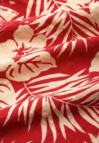 Czerwony materiał z wzorem kwiatowym, przedstawiający kremowe kwiaty hibiskusa oraz liściaste motywy, charakteryzujący się gładką teksturą z delikatnym splotem.