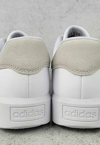 Sneaker bianche in pelle con un dettaglio in suede grigio sul tallone, dotate di una robusta suola bianca e del logo "adidas" in rilievo sul retro.