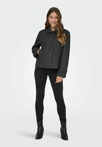 Šedá jarní bunda z vlněné směsi s límcem, předními knoflíky a bočními kapsami, nošena přes černé roztrhané úzké džíny a černé kotníkové boty.