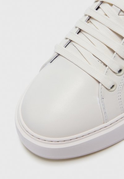 Sneaker bianco in pelle con texture liscia, punta rotonda e lacci in cotone piatti. Presenta cuciture sottili e una suola in gomma grigia.