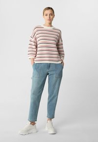 Sweter w paski w kolorze kremowym, burgundowym i granatowym; luźny krój. Jasnoniebieskie dżinsy z kieszeniami bocznymi. Białe sneakersy. Prosty design.