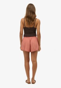 Top corto de punto marrón oscuro con tirantes finos, combinado con pantalones cortos sueltos de color rosa claro. Textura suave y detalle de dobladillo con forma de concha.