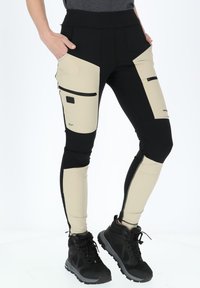 Svart och beige leggings i stretchigt material, med flera fickor, dragkedjor och kontrasterande färgpaneler längs benen.