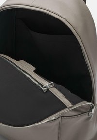 Mochila de cuero gris con apertura con cremallera, que cuenta con un interior de tela negra y un bolsillo adicional en el interior. Textura suave y diseño minimalista.
