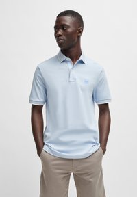 Šviesiai mėlynas polo marškinėlis, pagamintas iš minkštos medžiagos, turi klasikinį apykaklę, trumpas rankoves ir mažą logotipą krūtinėje. Tvarkingas pritaikymas.