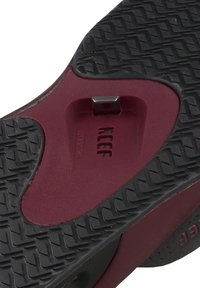 Black rubber sandal sole with textured surface. Burgundy upper section with a recessed area for a plug or attachment. Features logo embossed.