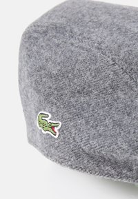 Gray wool beret with a soft, textured finish. Features a green embroidered crocodile logo on the side. Rounded shape.