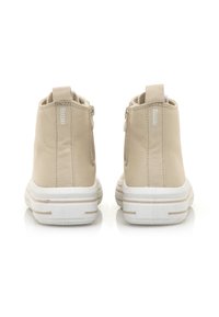 Botas de tobillo de lona beige con cierre de cremallera, suela de goma blanca en contraste y un detalle de marca minimalista en la parte trasera.