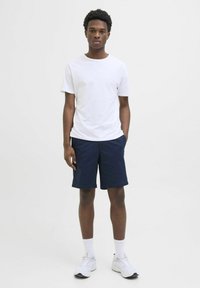 Hvid t-shirt med korte ærmer, marineblå shorts, hvide træningssko og hvide sokker. Simpelt design, afslappet pasform og åndbart stof.