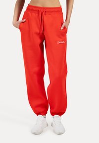 Červené teplákové kalhoty s elastickým pasem, stahovací šňůrkou a žebrovanými manžetami. Na levém stehně se nachází detail bílého loga. Vyrobeno z měkkého materiálu.