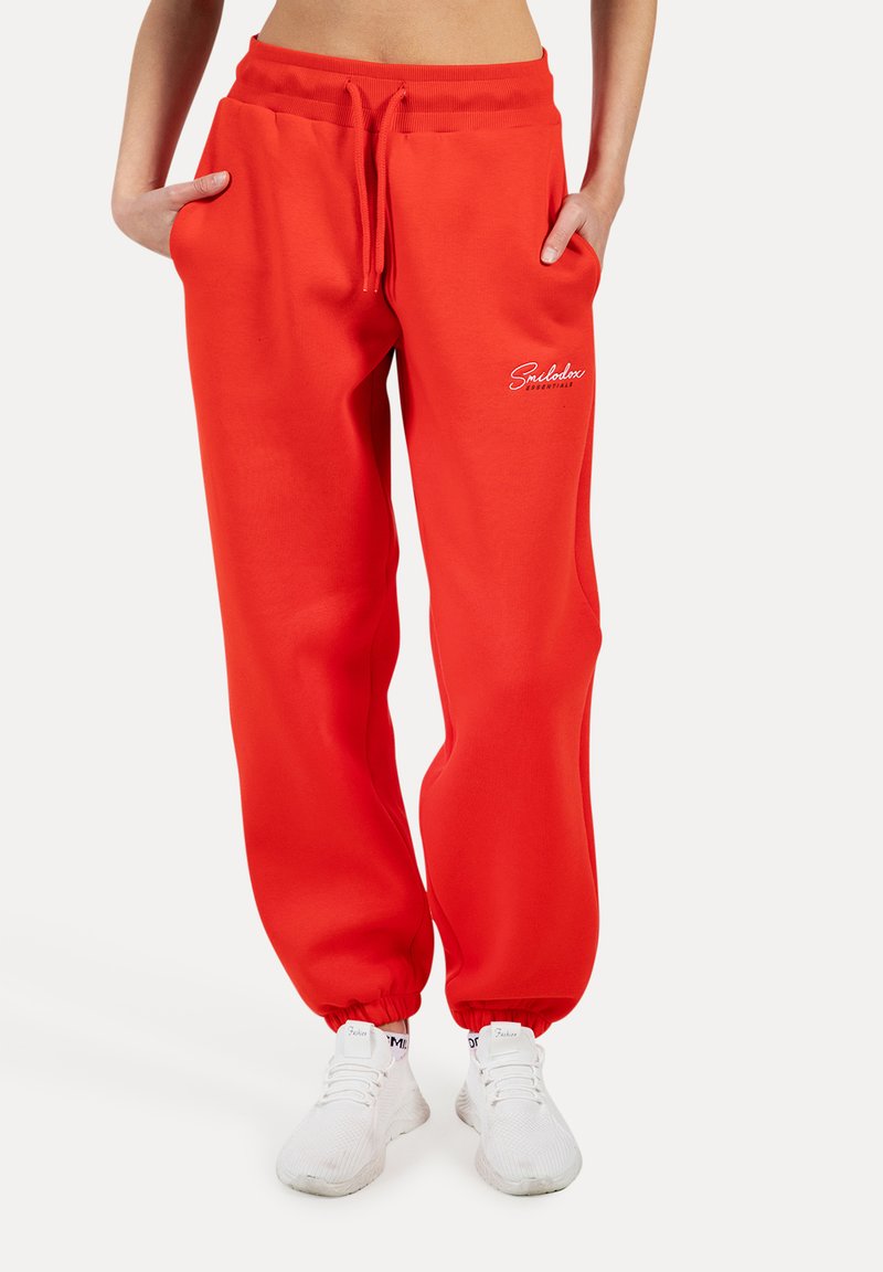 Červené teplákové kalhoty s elastickým pasem, stahovací šňůrkou a žebrovanými manžetami. Na levém stehně se nachází detail bílého loga. Vyrobeno z měkkého materiálu.