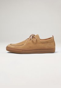 Zapatos de ante color crema con punta redondeada, diseño de cordones y suela de goma de contraste. Detalles de costura sutil y marca en el lado.