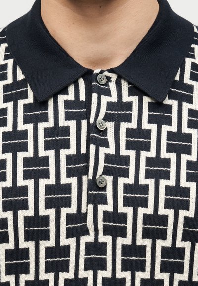 Πλεκτό πόλο πουκάμισο σε ασπρόμαυρο με γιακά, με γεωμετρικό ορθογώνιο μοτίβο και τρία μαύρα κουμπιά στη μπροστινή πατιλέτα.