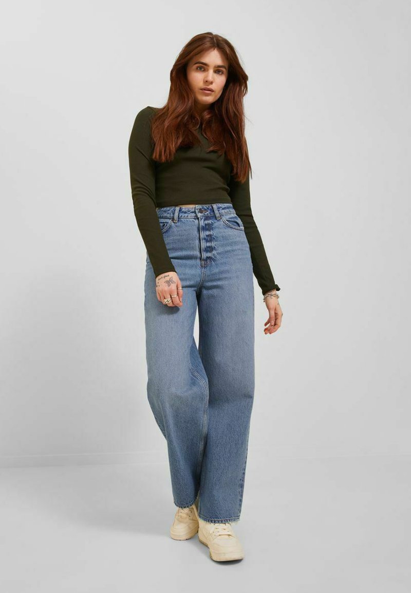 Jeans in denim azzurro chiaro a vita alta con una vestibilità a gamba larga e un leggero sbiadimento, abbinati a un top fitted a maniche lunghe di colore verde scuro.