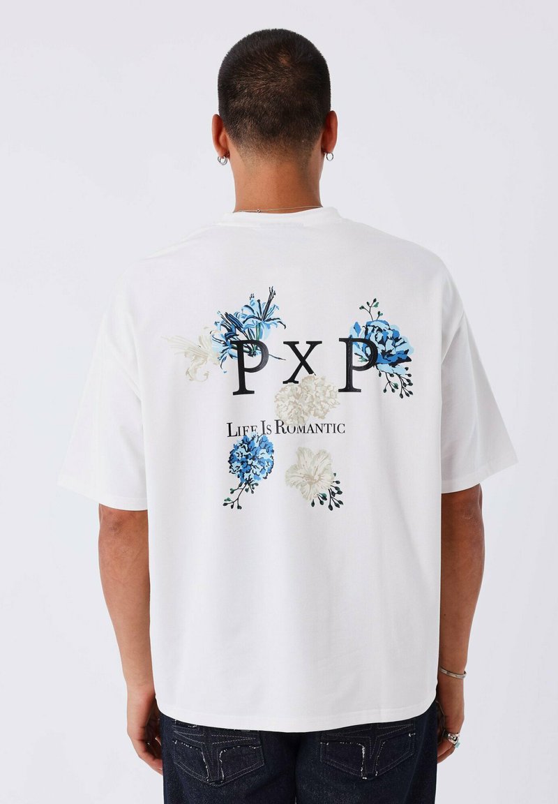 Camiseta de algodón blanca con estampados florales en azul y verde, logo negro "PXP" y texto "La vida es romántica" en la parte posterior.