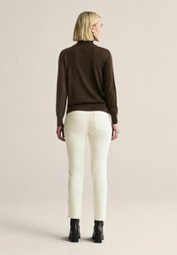 Brun stickad tröja, vita tajta byxor och svarta ankelboots. Tröjan har en hög krage; byxorna har bakfickor och en smal passform.