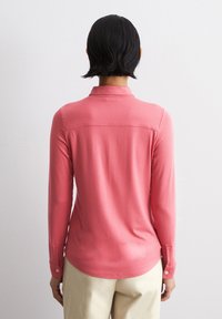 Langermet rosa skjorte med krage, med en glatt tekstur og knappede mansjetter, sett fra baksiden mot en nøytral bakgrunn.