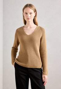 Pull en maille côtelée brun avec un col en V et des manches longues, fabriqué en tissu tricoté texturé, associé à un pantalon noir.