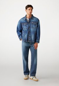 Lichtblauwe spijkerjacket met lange mouwen, voorzakken en een relaxte pasvorm, gecombineerd met bijpassende spijkerbroeken en sneakers.