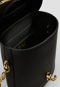 Schwarze Lederhandtasche mit runder Form, goldfarbener Hardware und offener Oberseite. Das Innere verfügt über ein Logo und mehrere Kartenfächer.