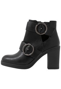 Schwarzer Absatz-Ankle-Boot aus Kunstleder. Verfügt über zwei breite Riemen mit kreisförmigen Metall-Schnallen und einem strukturierten Blockabsatz.