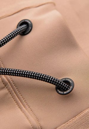 Tan tyg med en texturerad yta, förstärkt med svart- och vitt flätade drarepet samt metallöglor, vilket betonar hållbarhet och funktionalitet.