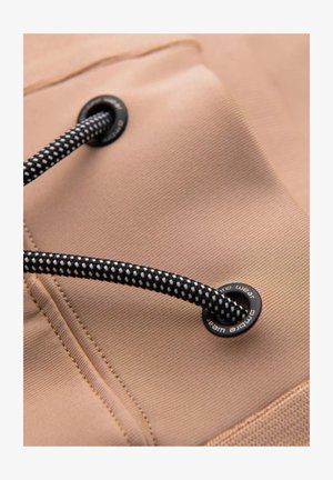 Un tissu beige avec une surface texturée présente des cordons tressés noir et blanc et des œillets en métal, mettant en avant la durabilité et la fonctionnalité.