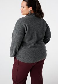 Grijze gebreide trui met een hoge kraag en geribbelde zoom. Gecombineerd met bordeauxrode broek. Gestructureerde stof geeft een zachte uitstraling.