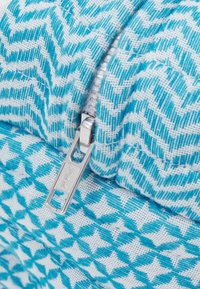 Bolsa con cremallera de patrones en zigzag azul y blanco y estrellas. Presenta un tirador de cremallera YKK plateado y un detalle de tela texturizada.