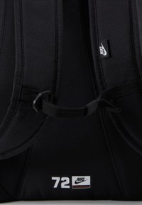 Black Nike backpack featuring padded straps, nylon material, and a label with "72" and Nike logo. Smooth texture with minimalistic design.