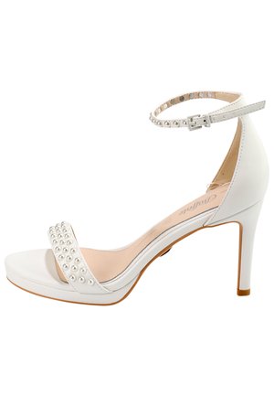 White high-heel sandal with an ankle strap, featuring a beaded accent across the front and a smooth, glossy finish. Slim stiletto heel.