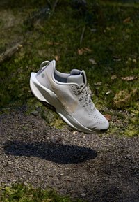 Baskets de course gris clair avec tige en mesh, accents contrastants et semelle texturée. Équipées de lacets et d'un logo sur le côté.
