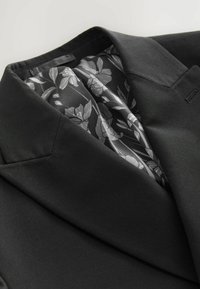 Blazer negro con solapa muestrada, tejido suave y un forro de satén gris con estampado floral visible en el interior.