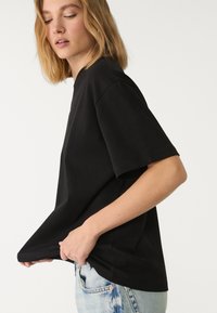 Sort bomulds T-shirt med korte ærmer, afslappet pasform, rund halsudskæring og glat tekstur. Båret med lyseblå denimjeans.