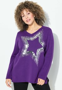 Maglione lungo viola con maniche lunghe, caratterizzato da un grande design di stella argentata con paillettes. Il tessuto ha una texture a coste, una vestibilità leggermente ampia e scollo a V.