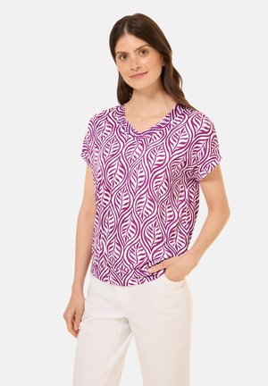 T-shirt med korte ærmer og v-hals, i et bladmønster med lilla og hvid, lavet af et let materiale, parret med hvide bukser.