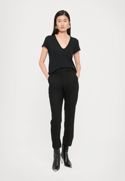 T-shirt nero con scollo a V realizzato in tessuto morbido, abbinato a pantaloni neri su misura con dettaglio a bottone. Stivali neri a punta al ginocchio.