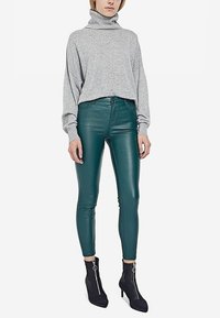 Grijze coltrui met lange mouwen, gecombineerd met hoge glanzende groene legging en zwarte enkellaarsjes met een ritsdetail.