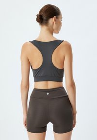 Mørkegrå sportsbh med racerback-design og bred bånd, parret med høj talje, mørkebrune shorts. Glat, strækbart stof.