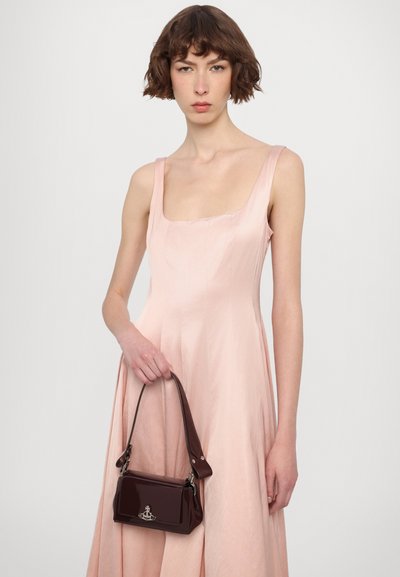 Roze, mouwloze jurk met een vierkante halslijn. Model houdt een kleine, donker bordeauxkleurige handtas van glanzend leer vast met een korte strap en logo-detail.