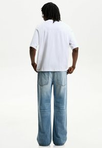 White cotton t-shirt with short sleeves, paired with light blue wide-leg jeans featuring a faded texture and back pockets.