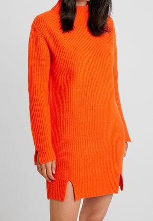 Robe pull orange tricotée avec un col montant, des manches longues, une texture côtelée, des fentes latérales et une coupe décontractée.