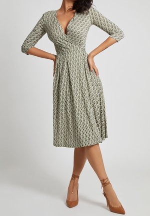 Knee-length wrap dress in light green with geometric pattern, 3/4 sleeves, and a V-neckline, paired with tan high-heeled shoes.