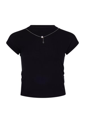 Top nero a maniche corte con polsini arrotolati, abbinato a una sottile collana d'argento con una singola perla e un piccolo ciondolo pendente.