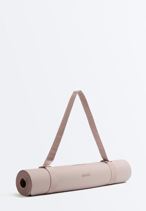 Beżowa zwinięta mata do jogi z teksturowaną powierzchnią i paskiem do przenoszenia, ustawiona pionowo na białym tle.