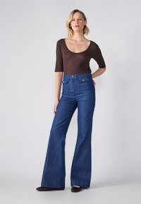 Σκούρο καφέ κοντομάνικο πουκάμισο με στρογγυλή λαιμόκοψη, συνδυασμένο με ψηλόμεσα μπλε καμπάνα τζιν που διαθέτουν δύο μπροστινές τσέπες και ασημένια κουμπιά.