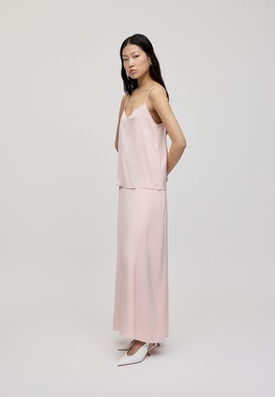 Lyserosa sateng-camisole kombinert med et matchende langt skjørt. Har justerbare tynne stropper, en jevn tekstur og en flytende silhuett.