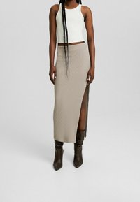 Vit räfflad kort topp i kombination med en beige räfflad maxijurk med en sidospalt, kompletterad med bruna stövlar över knäet.