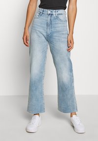 Ljusblå vida jeans med hög midja, tillverkade av denim. Har dragkedja, framfickor och en ren fåll. Stylar med vita sneakers.