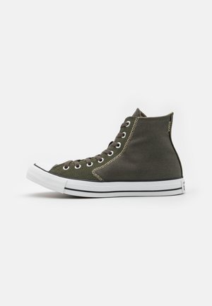 Mørkegrøn højtop canvas sneaker med hvid gummisål og sort stribe, hvid tåhætte og mørke snørebånd på ensfarvet baggrund.